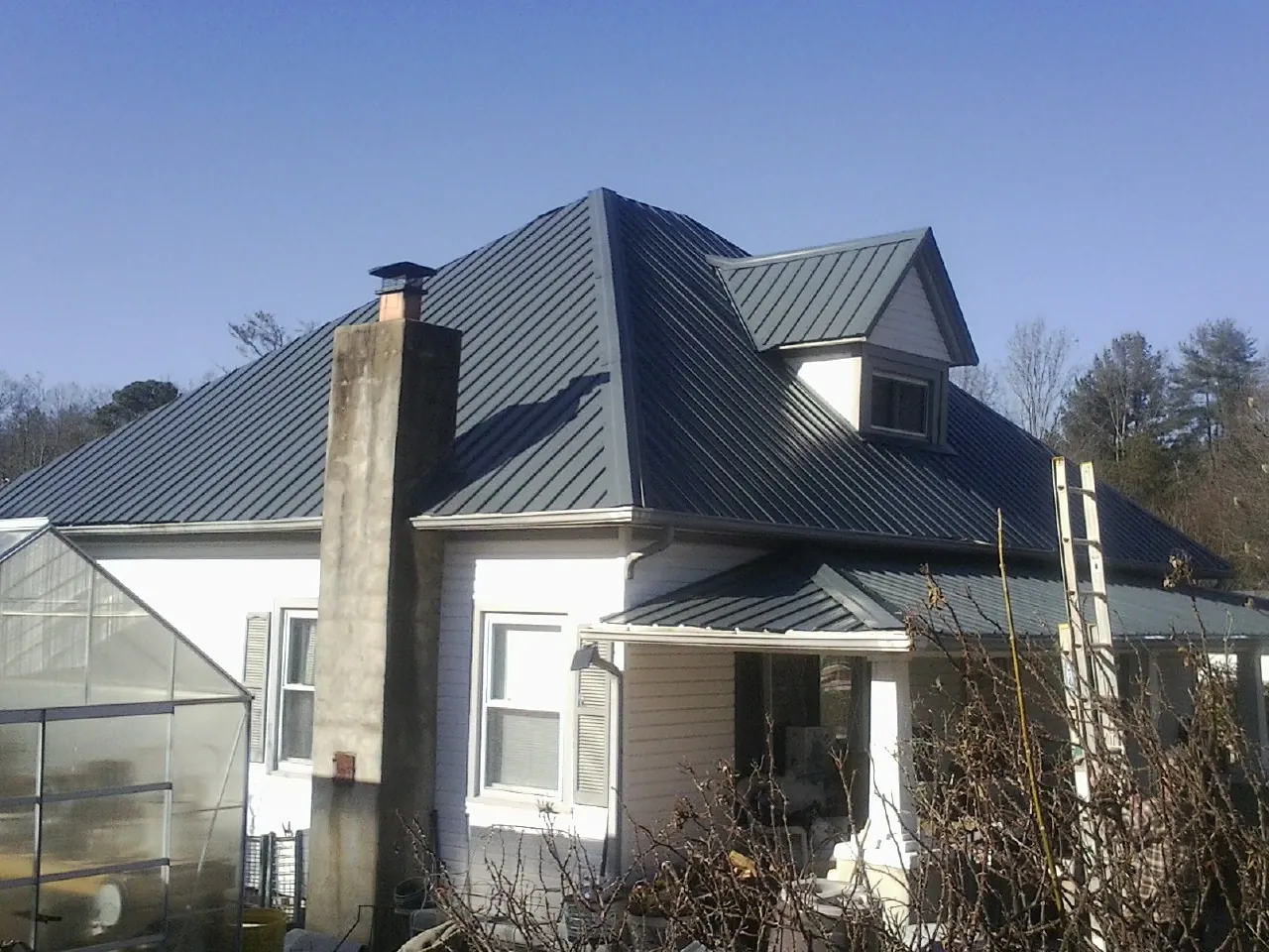 Dark blue standing seam metal roof on a white farmhouse with dormer — Slate & Tile Roof Repair by Roofing Brothers in Crescent Mills