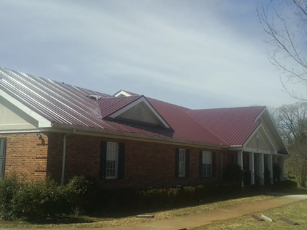 Red metal roof with gabled entries on a long brick building, from a Hail Damage Roof Repair job in Crescent Mills