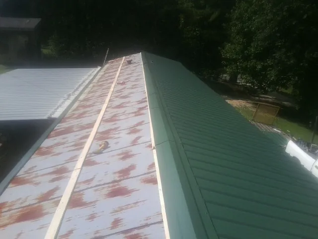Old rusted panels beside newly installed green metal roofing — Wind Damage Roof Repair by Roofing Brothers in Crescent Mills