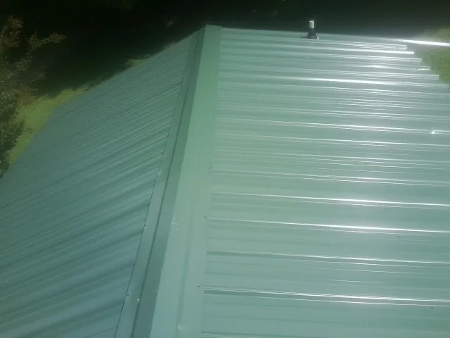 New green metal panels meeting at the ridge of a roof — Flat Roof Repair work by our crew in Crescent Mills