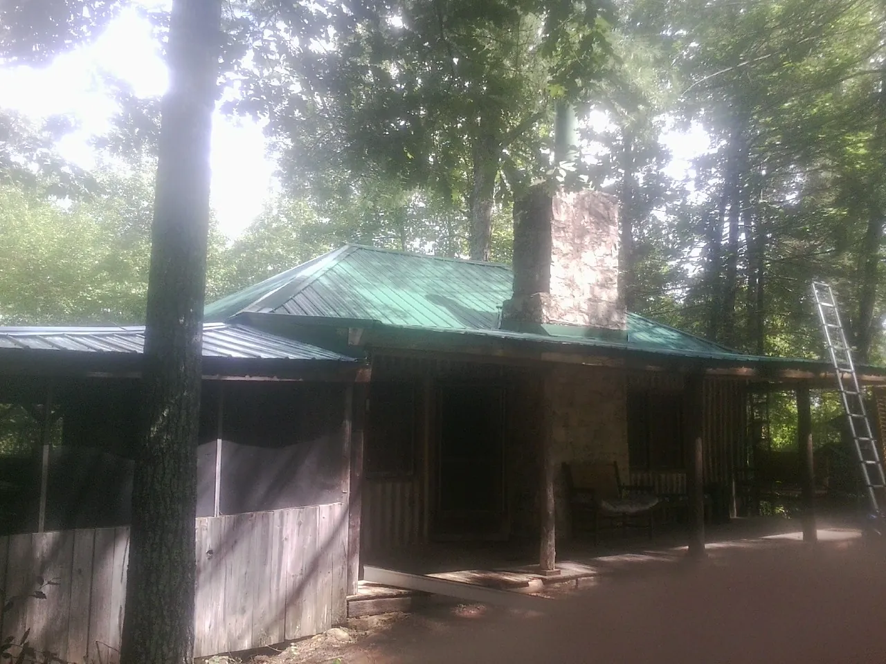 Green metal roof and stone chimney above a log cabin porch in Crescent Mills
