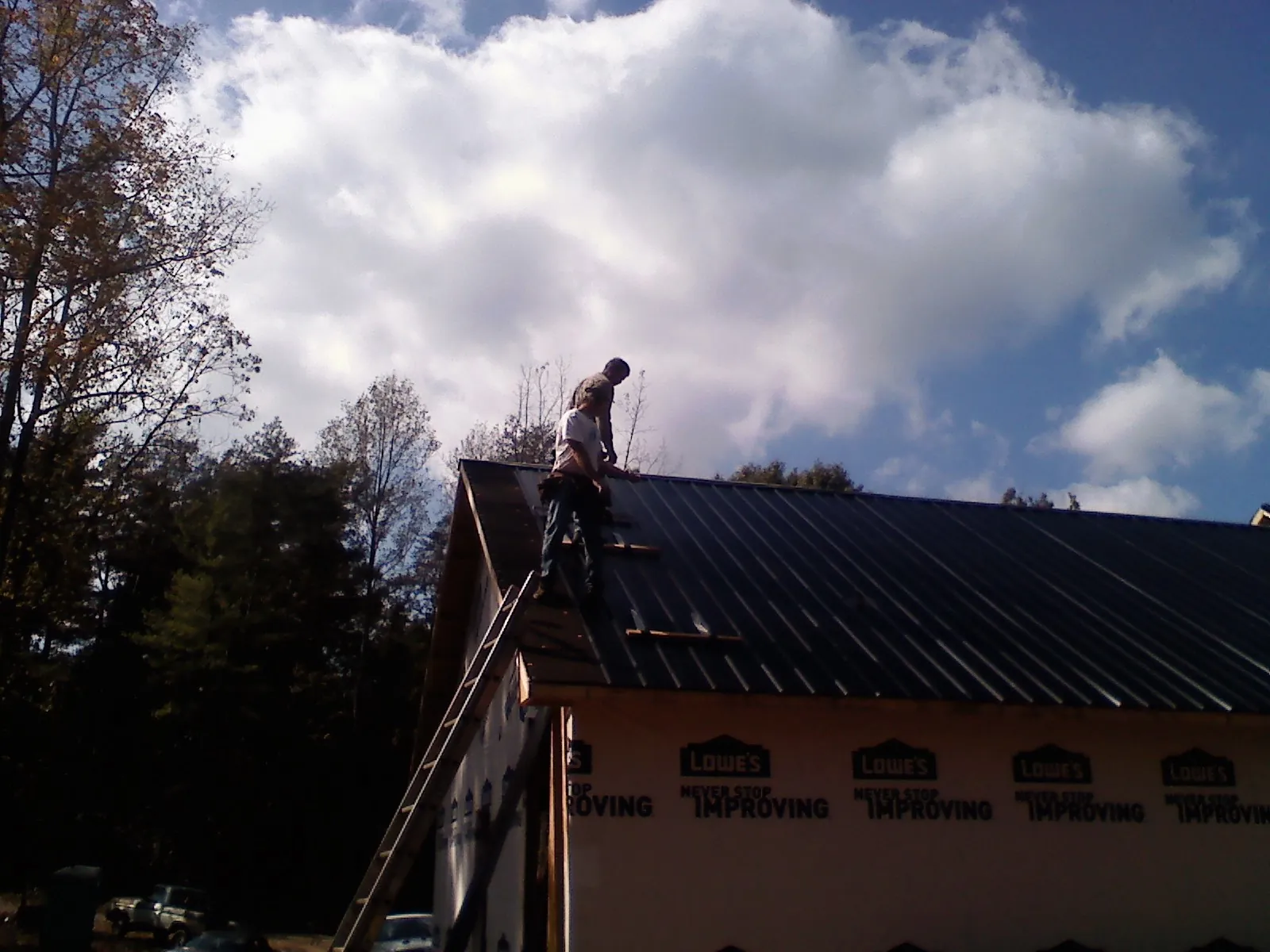 Roofer fastening dark metal panels high against a cloudy sky, from a Roof Inspection job in Crescent Mills