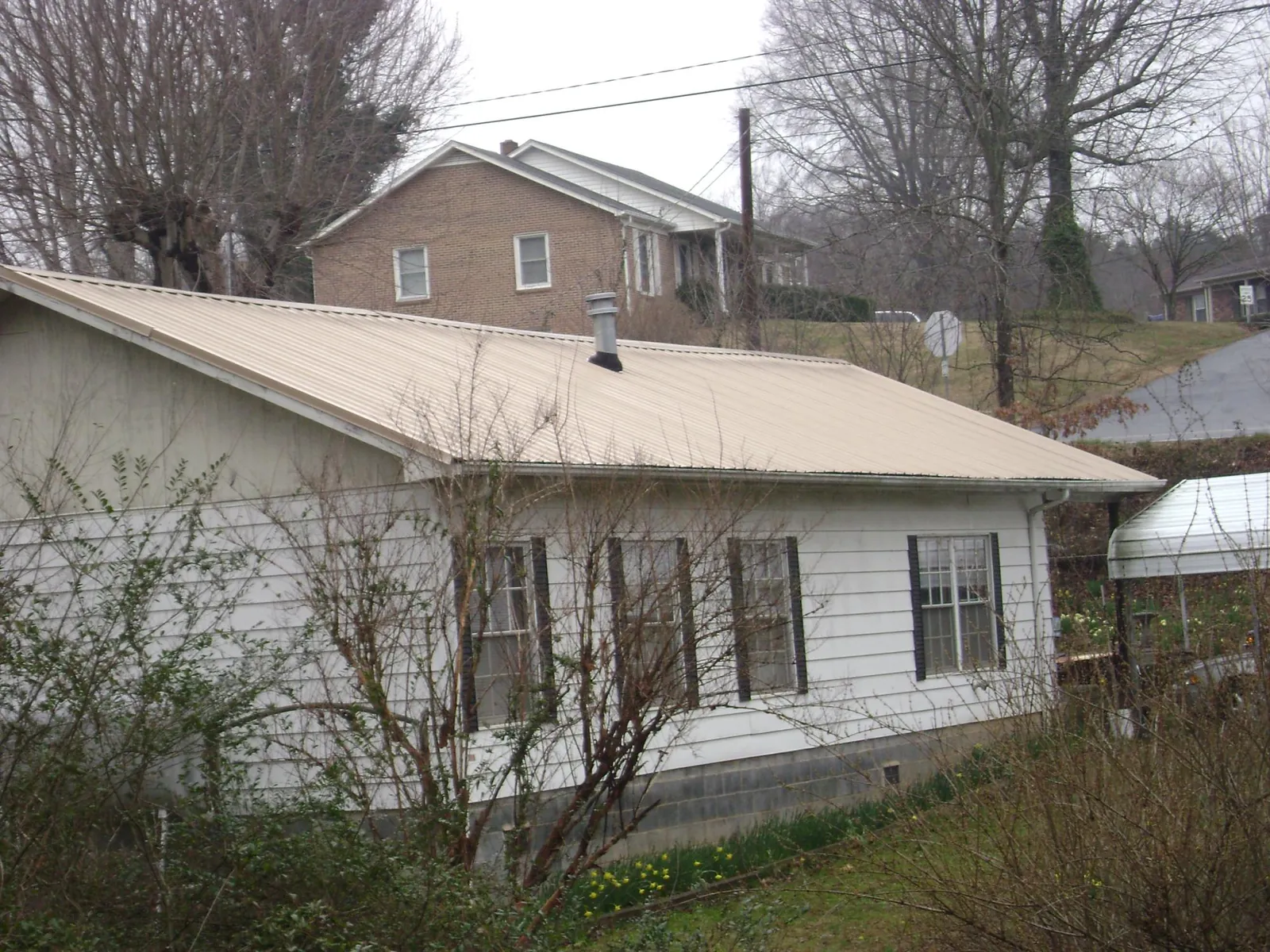 Tan metal roof on a white sided house set into a hillside — Commercial Roofing by Roofing Brothers in Crescent Mills