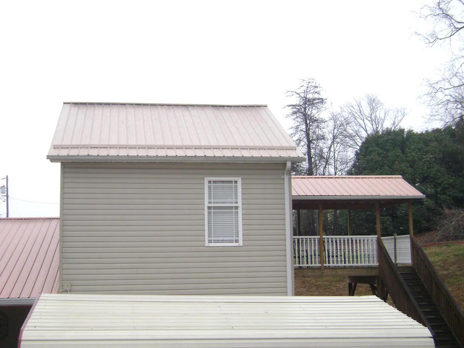 Tan metal roofs on a two story addition and attached porch, from a Roof Replacement job in Crescent Mills